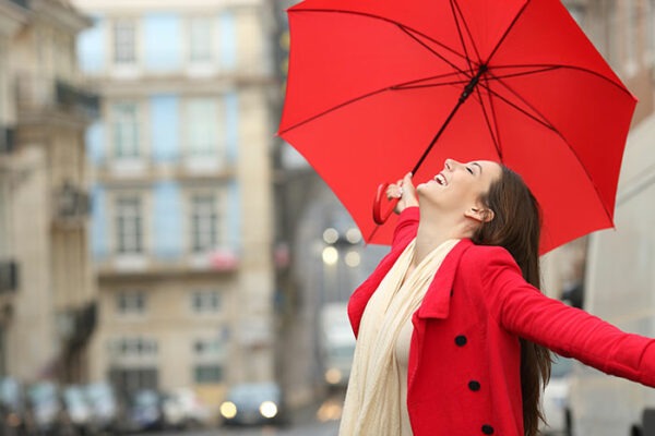 A woman wearing a red coar looking happy with a red umbrella