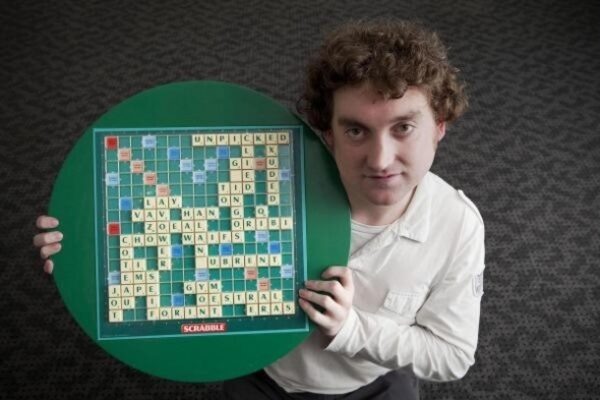 man holding up a scrabble board with tiles on it