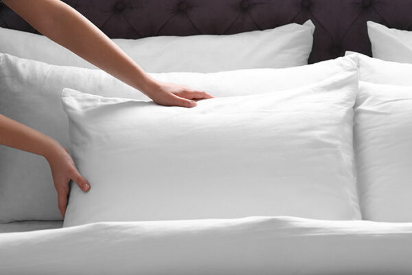 woman plumping up white pillow on bed