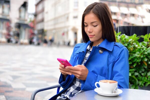 woman texting on a pink phone, sitted at table at a cafe, with a coffee